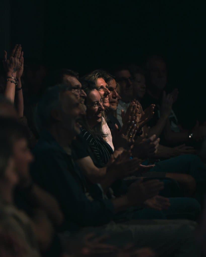 Audience members smiling and clapping at a live show.